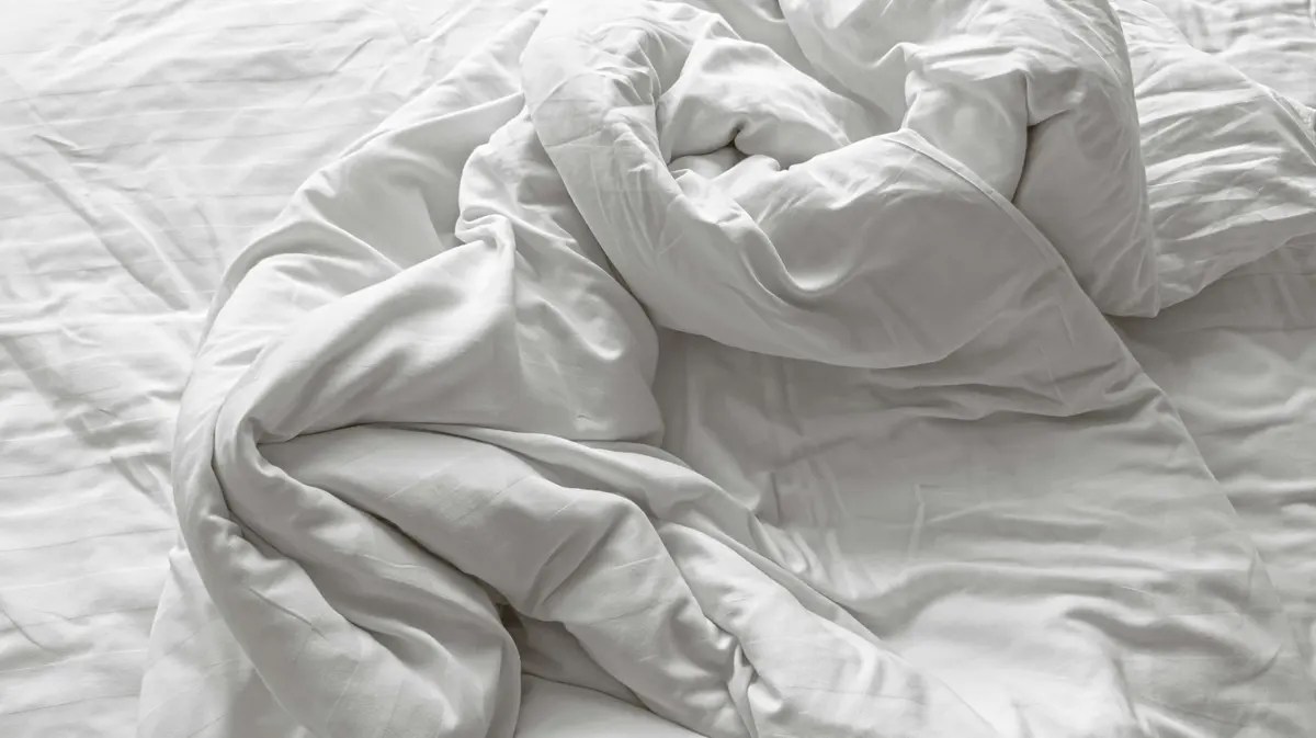 An unmade bed with white sheets and pillows