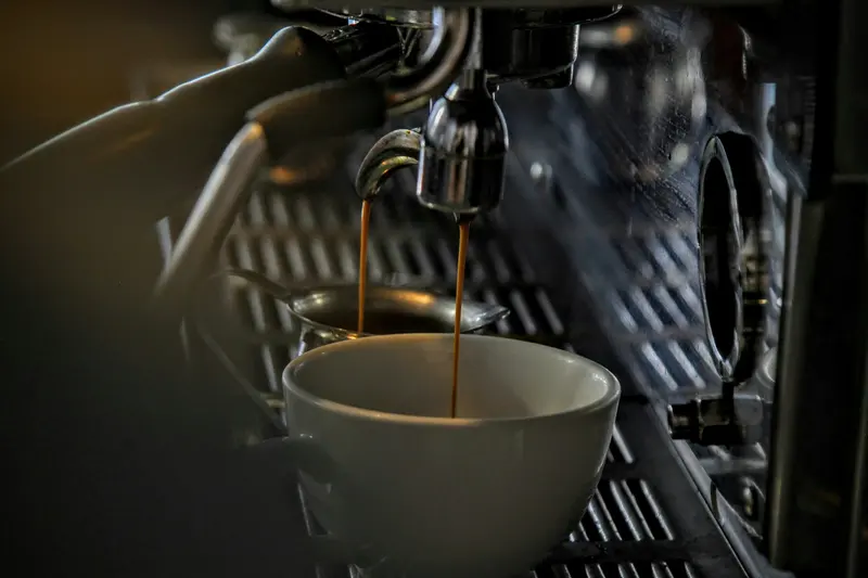 Espresso pouring into a small cup from a steel machine
